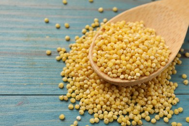 Photo of Spoon with millet groats on blue wooden table, closeup. Space for text