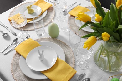 Photo of Festive table setting with glasses, burning candle and vase of tulips. Easter celebration