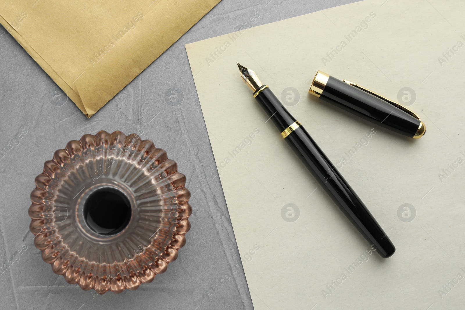 Photo of Stylish fountain pen, inkwell, envelope and paper on grey textured table, flat lay