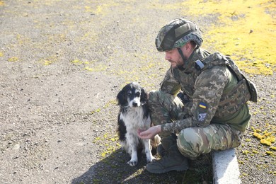 Photo of Ukrainian soldier with stray dog outdoors on sunny day. Space for text