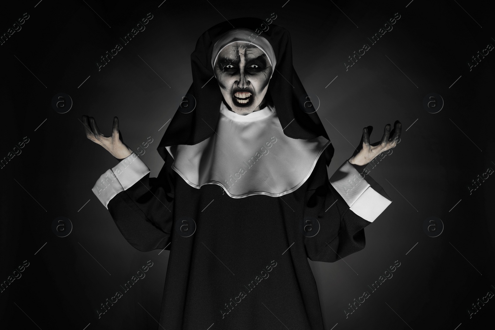 Photo of Portrait of scary devilish nun on black background. Halloween party look