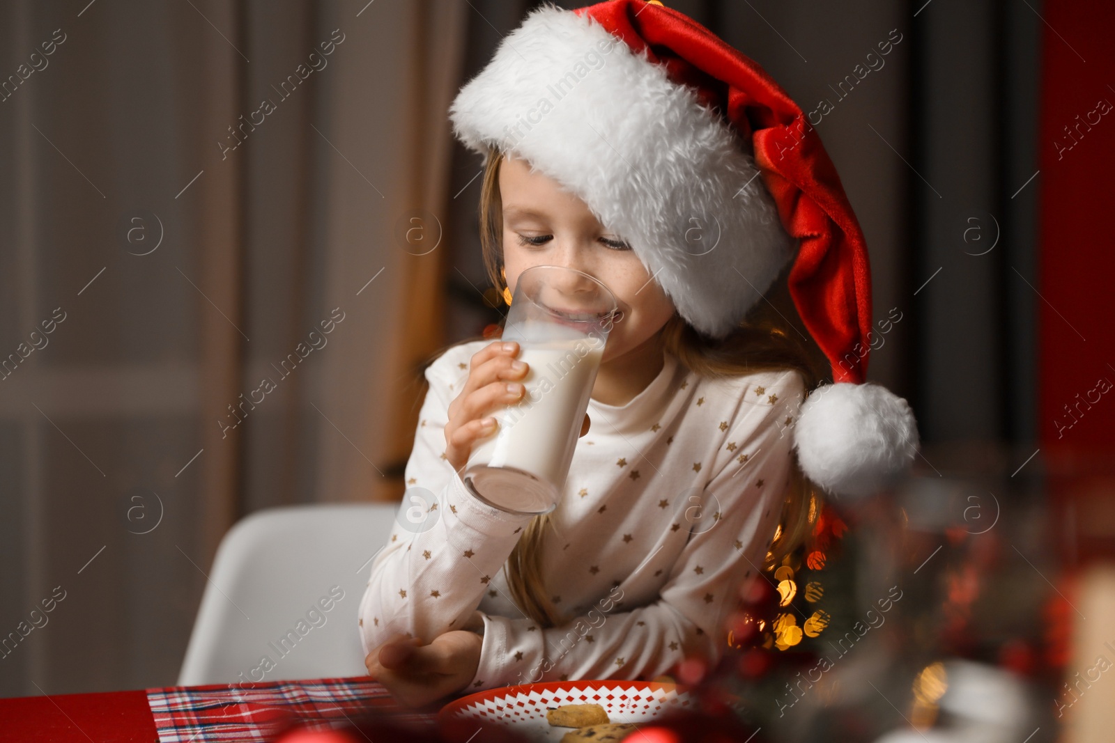 Photo of Cute little child drinking milk at table in dining room. Christmas time