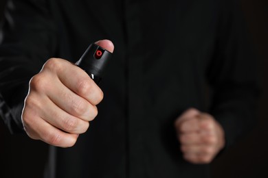 Man using pepper spray on black background, closeup. Space for text