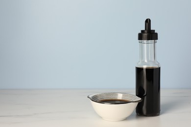 Bottle and bowl with soy sauce on white table, space for text