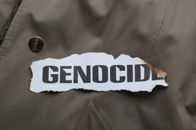 Piece of burnt paper with word Genocide on grey jacket, top view