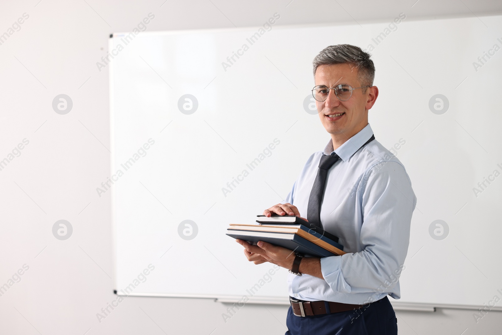 Photo of Teacher with notebooks near whiteboard in classroom