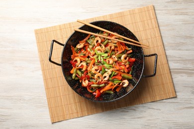 Photo of Shrimp stir fry with vegetables in wok and chopsticks on wooden table, top view