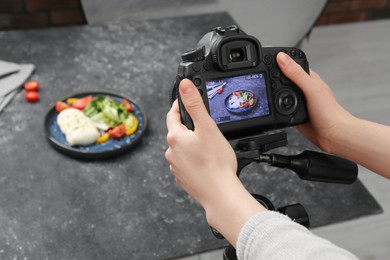 Woman taking picture of mozzarella salad on table in professional photo studio, closeup. Food photography