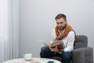 Photo of Handsome man reading magazine in armchair at home
