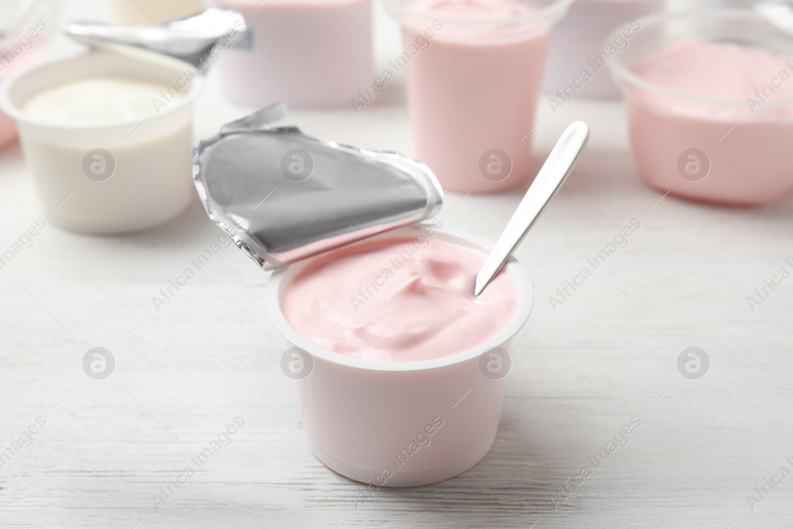 Photo of Plastic cup with fresh yogurt and spoon on white wooden table