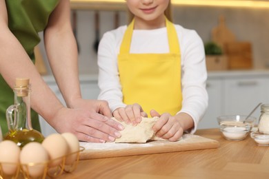 Photo of Making bread. Mother and her daughter kneading dough at wooden table in kitchen, closeup