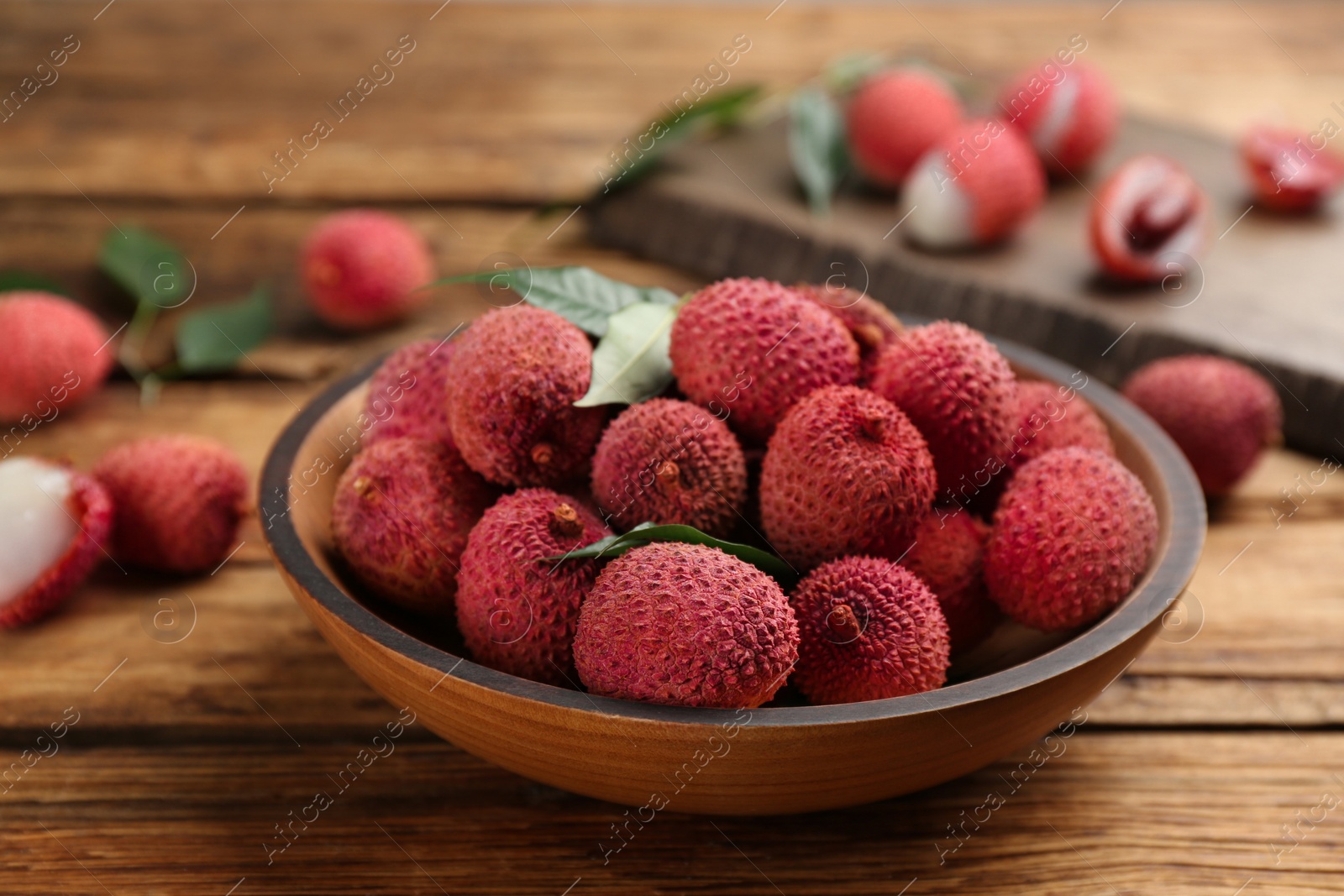 Photo of Fresh ripe lychee fruits in bowl on wooden table