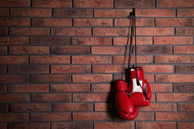 Photo of Pair of red boxing gloves hanging on brick wall, space for text