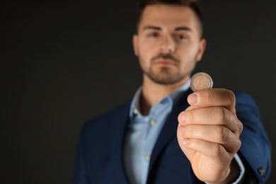 Young man holding coin against black background, focus on hand. Space for text