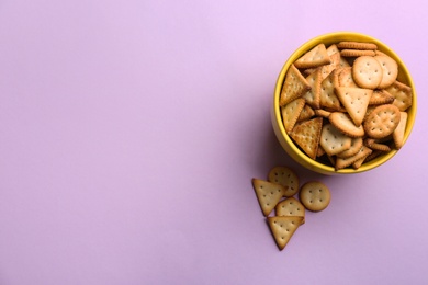 Photo of Delicious crackers in bowl on violet background, flat lay. Space for text
