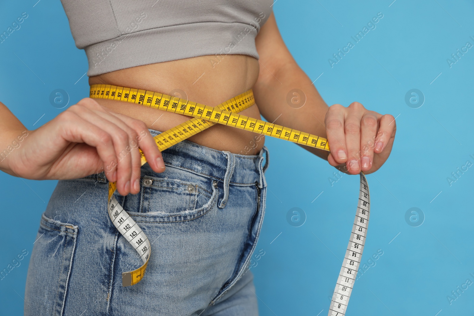 Photo of Woman measuring waist with tape on turquoise background, closeup