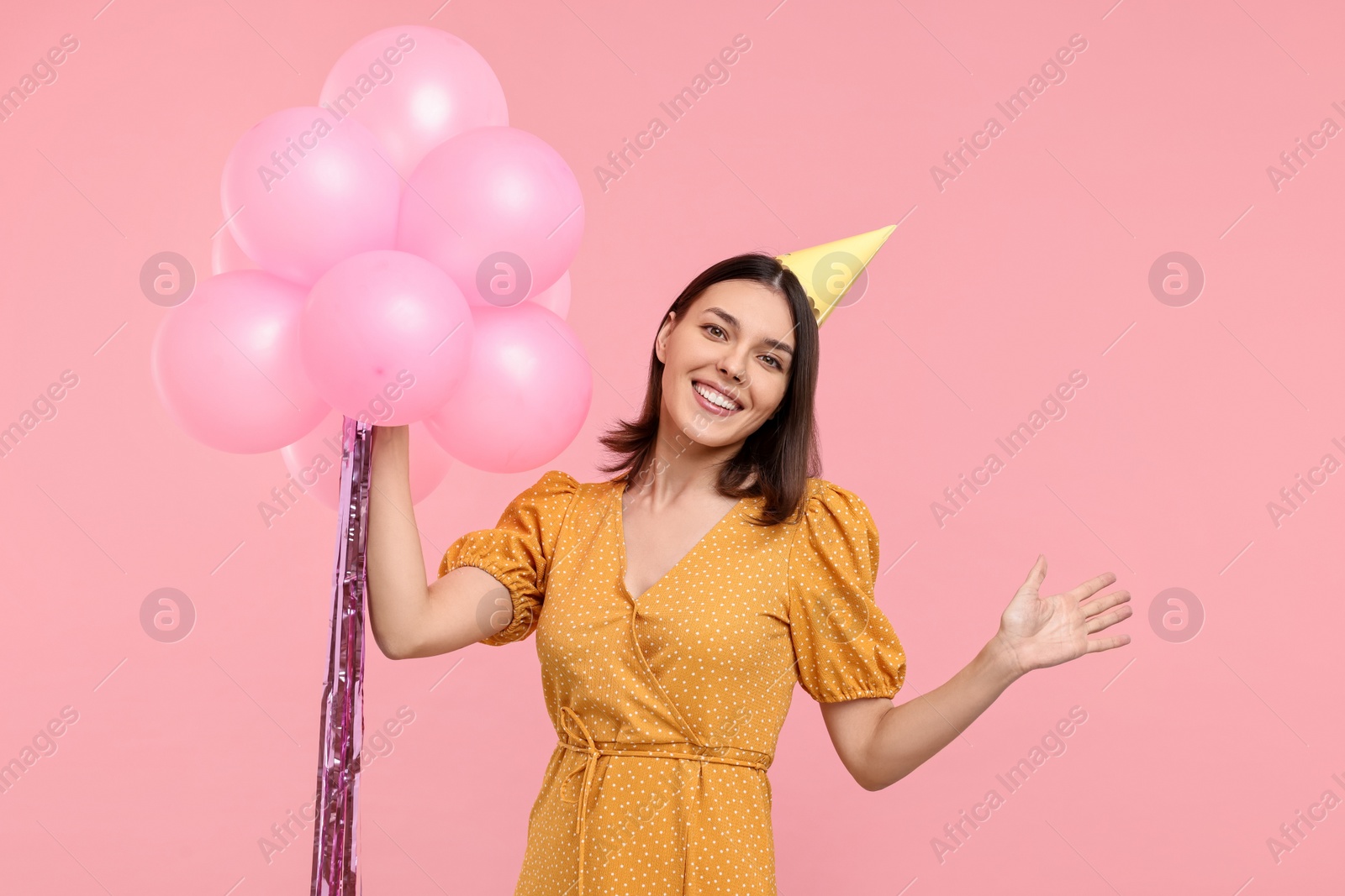 Photo of Happy young woman in party hat with balloons on pink background