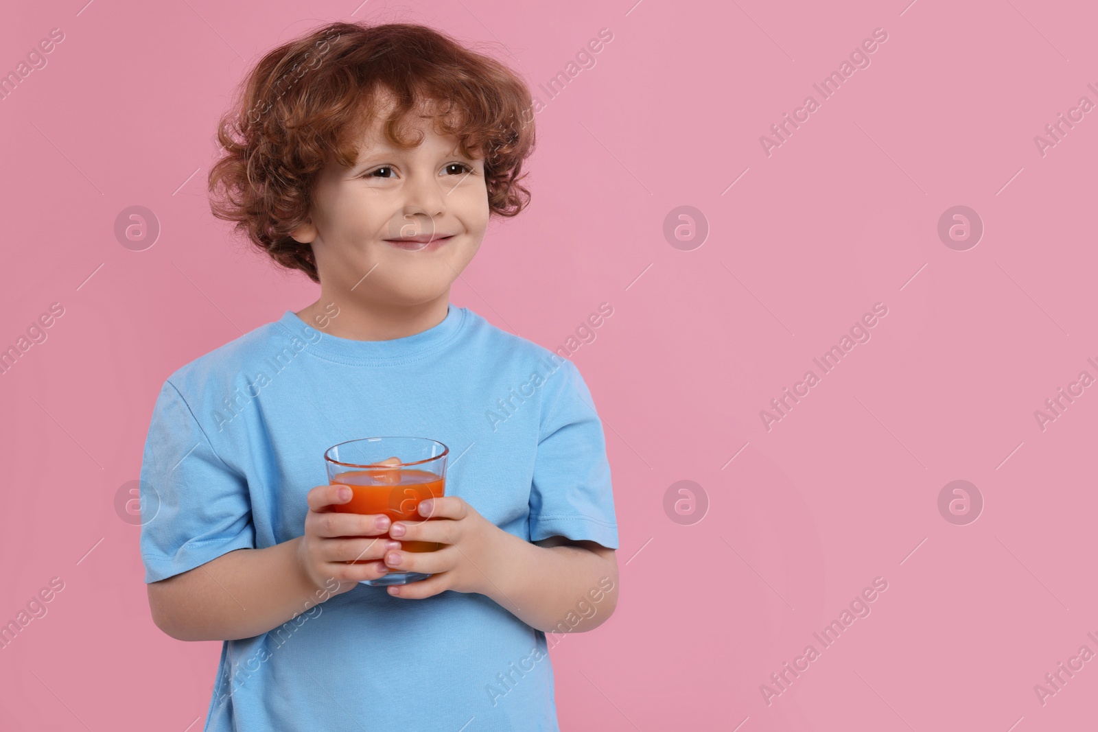 Photo of Cute little boy with glass of fresh juice on pink background, space for text