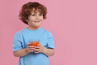 Photo of Cute little boy with glass of fresh juice on pink background, space for text