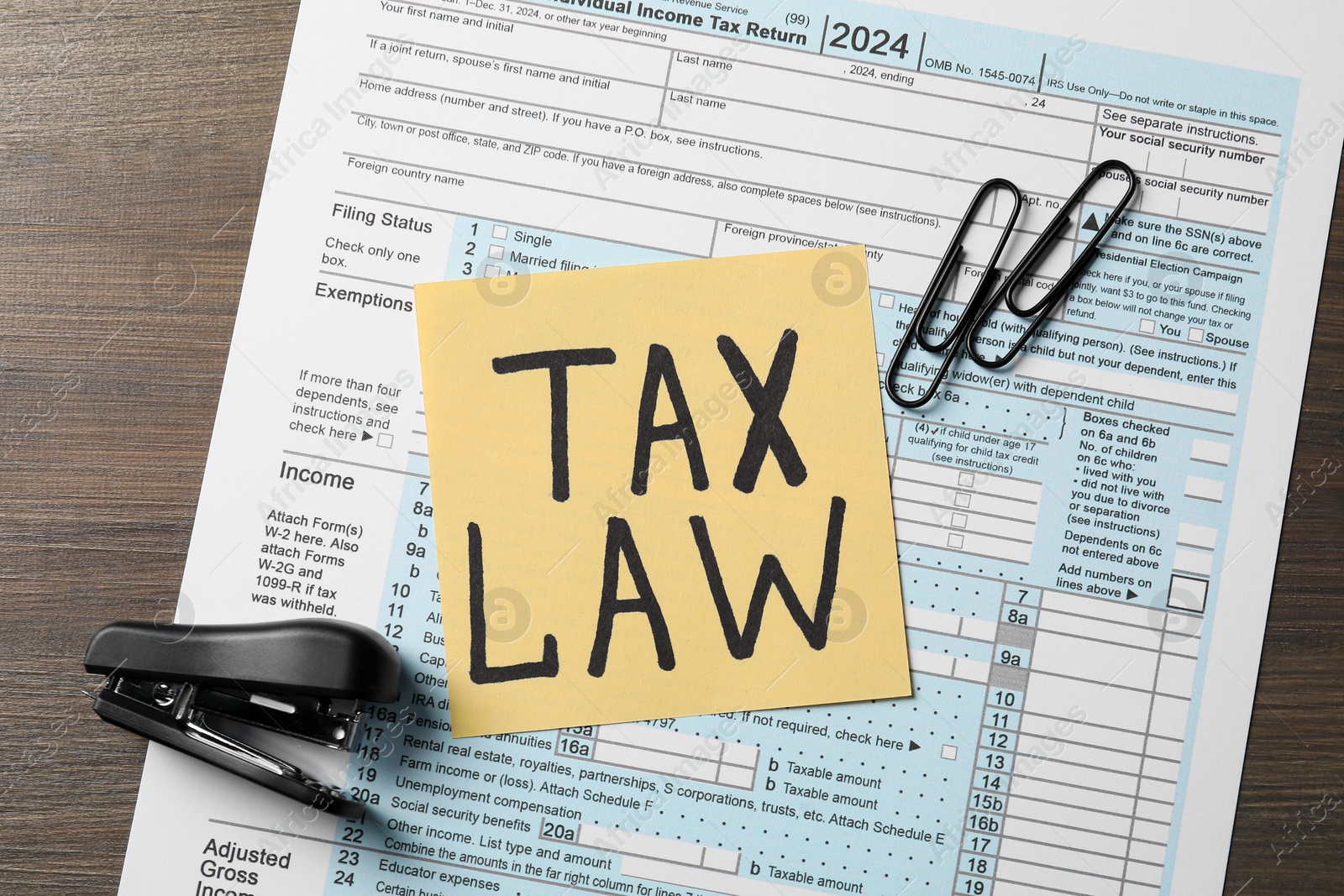 Photo of Note with words Tax Law, form, stapler and paper clips on wooden table, top view