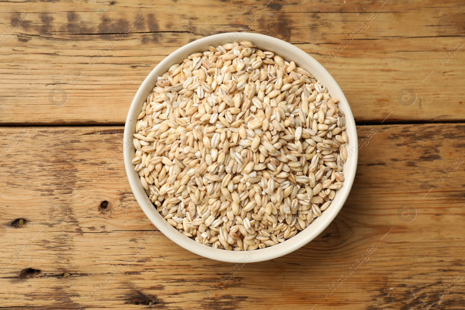 Photo of Dry pearl barley in bowl on wooden table, top view