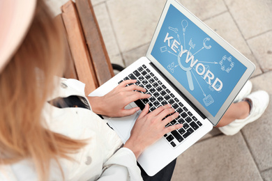Image of Keywords research concept. Woman working with laptop on bench outdoors, above view