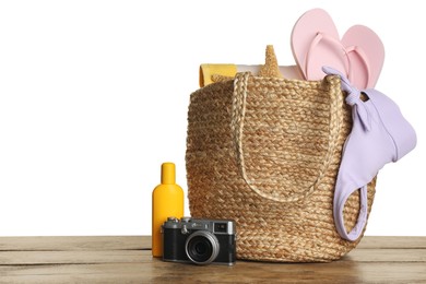 Bag with different beach objects on wooden table against white background