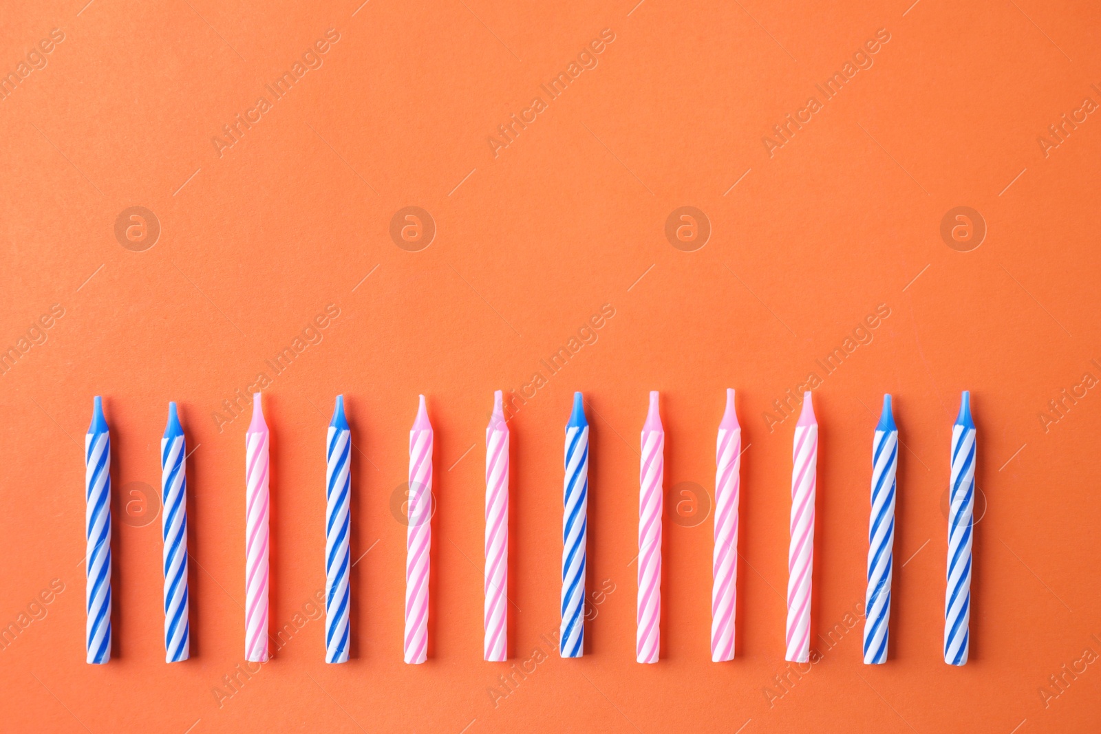 Photo of Colorful striped birthday candles on orange background, flat lay. Space for text