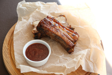 Photo of Delicious grilled pork ribs and sauce on wooden board