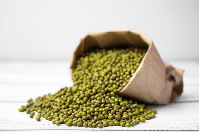 Photo of Paper bag with green mung beans on white wooden table, closeup