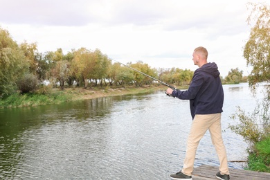 Photo of Man fishing on wooden pier at riverside. Recreational activity