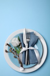 Photo of Festive table setting with willow twigs and tulip on light blue background, top view. Easter celebration