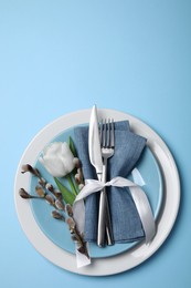 Festive table setting with willow twigs and tulip on light blue background, top view. Easter celebration