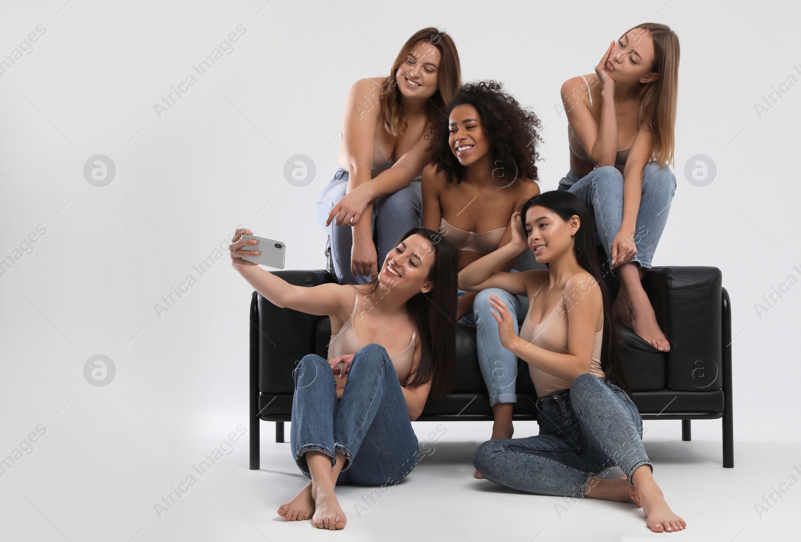 Photo of Group of women with different body types in jeans and underwear taking selfie against light background