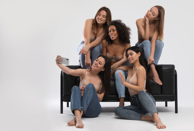 Photo of Group of women with different body types in jeans and underwear taking selfie against light background