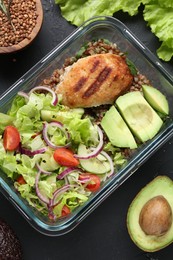 Healthy meal. Fresh salad, avocado, cutlet and buckwheat in glass container near other products on black table, flat lay