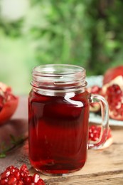 Photo of Pomegranate juice in mason jar and fresh fruits on wooden table outdoors