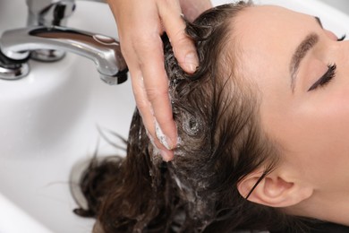 Photo of Professional hairdresser washing client's hair at sink, closeup