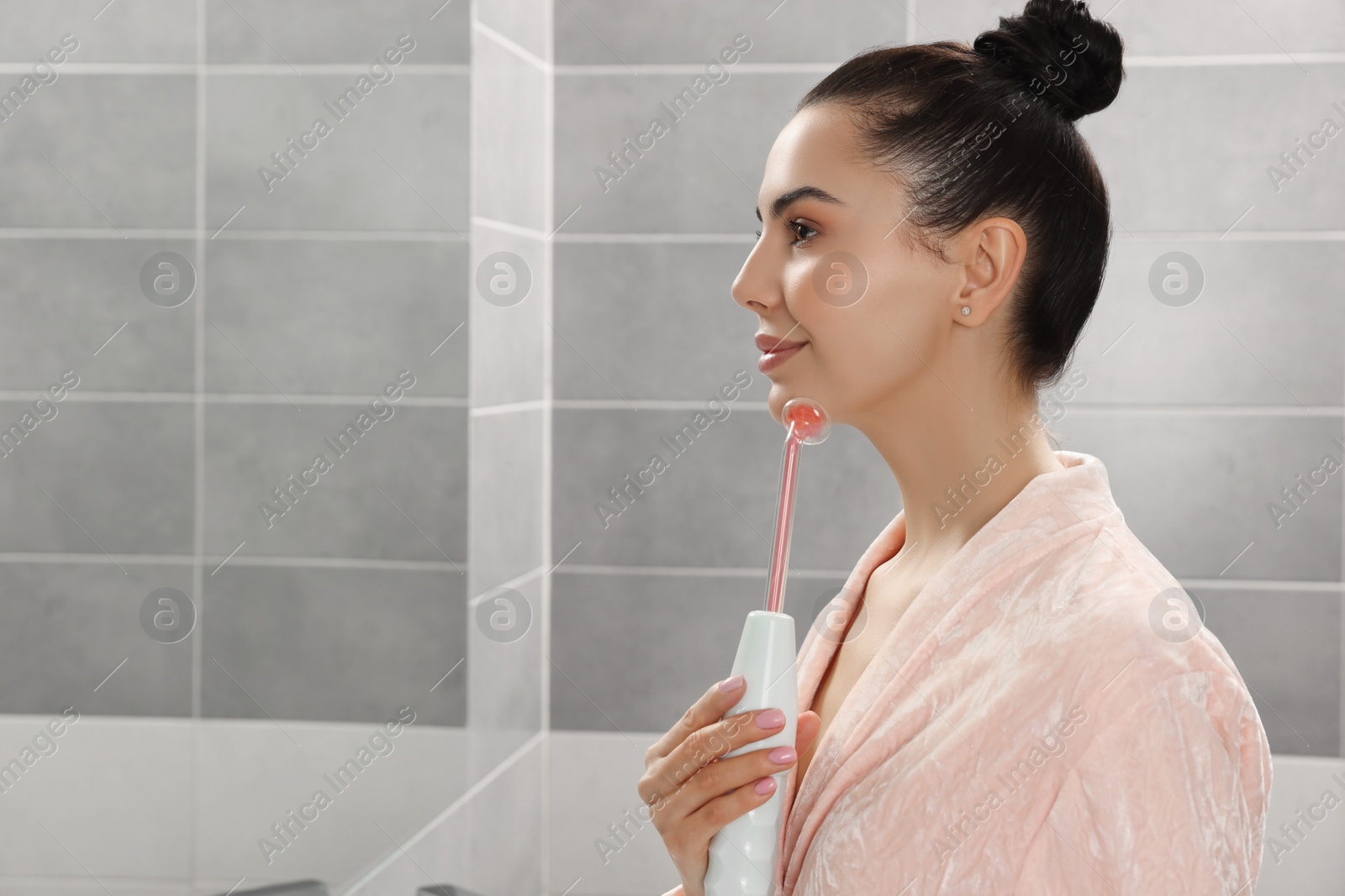 Photo of Woman using high frequency darsonval device in bathroom, space for text