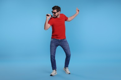 Photo of Handsome man with sunglasses and microphone singing on light blue background