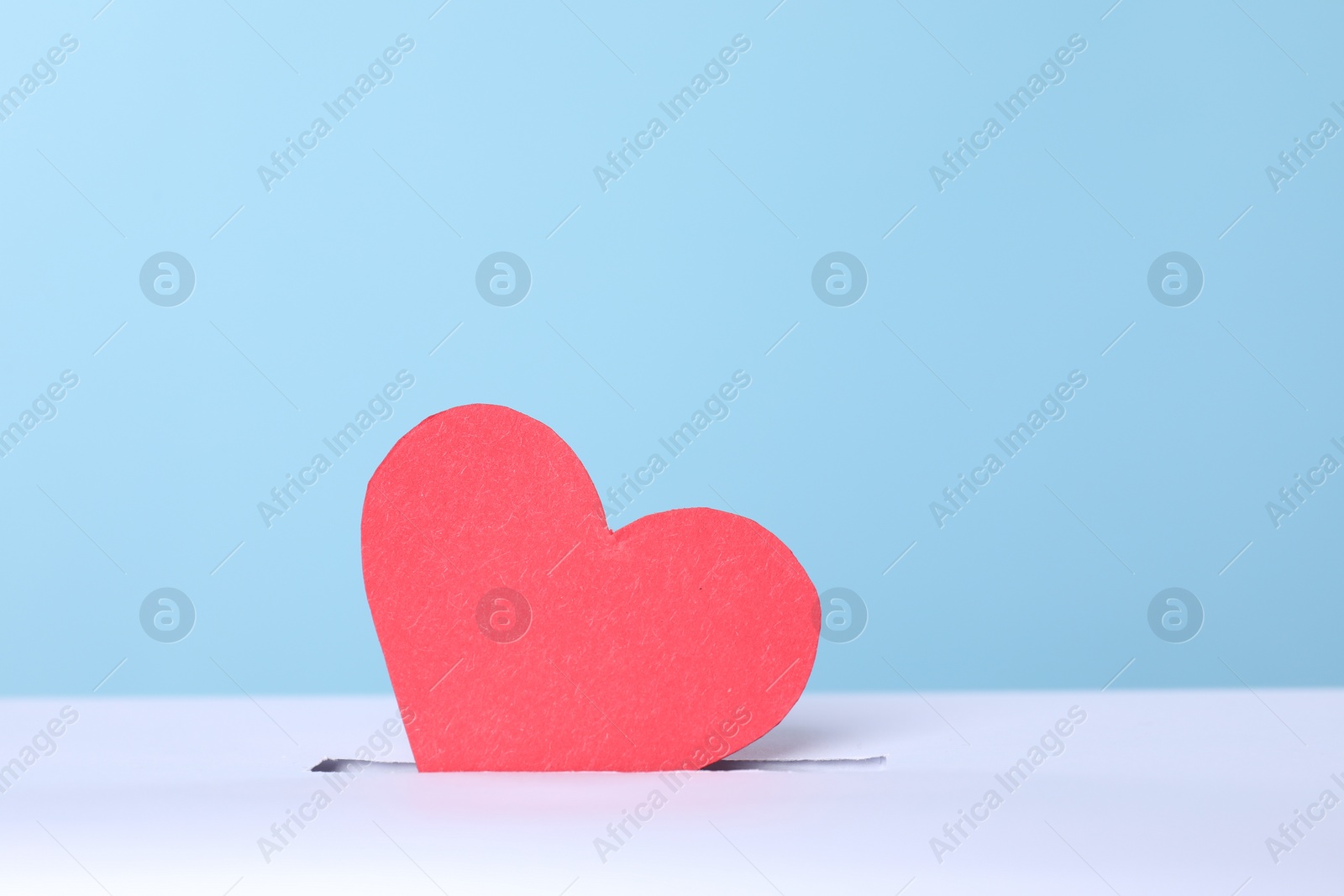 Photo of Red heart into slot of donation box against light blue background