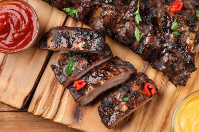Tasty grilled ribs and sauces on wooden table, flat lay