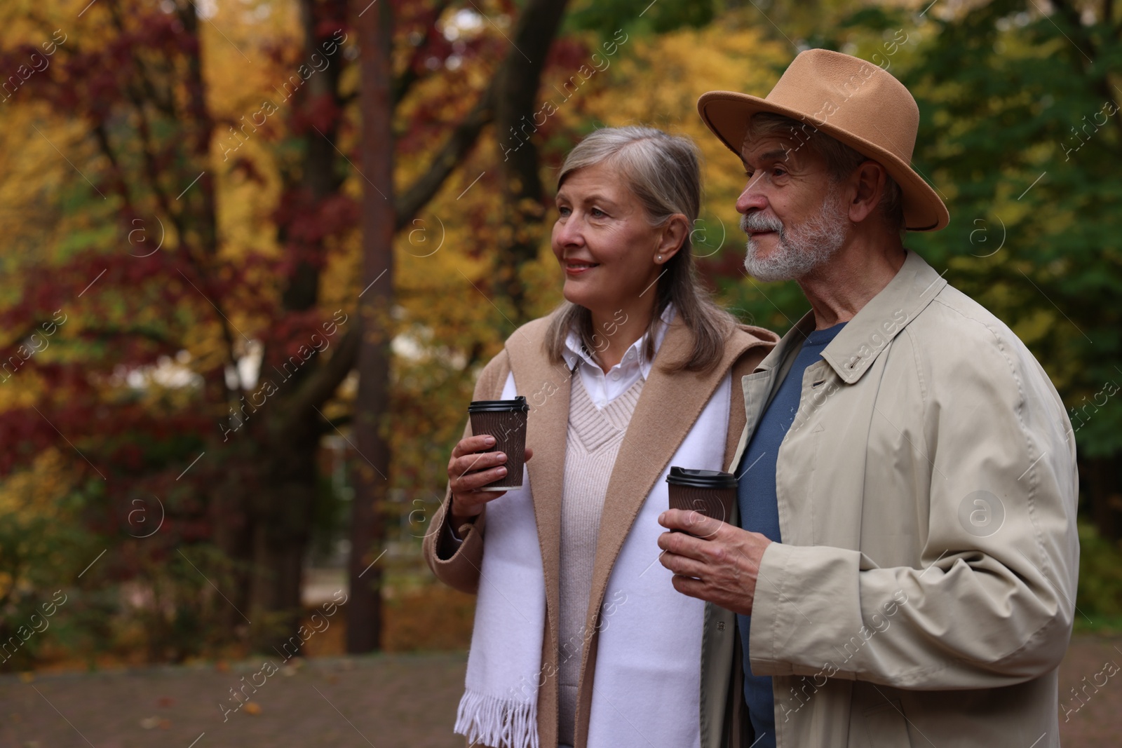 Photo of Affectionate senior couple with cups of coffee in autumn park, space for text