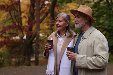 Photo of Affectionate senior couple with cups of coffee in autumn park, space for text