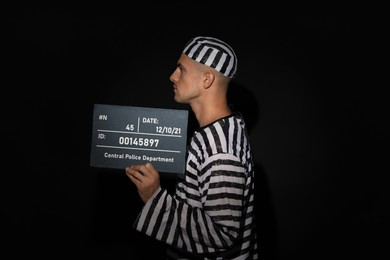Photo of Mug shot of prisoner in striped uniform with board on black background, side view