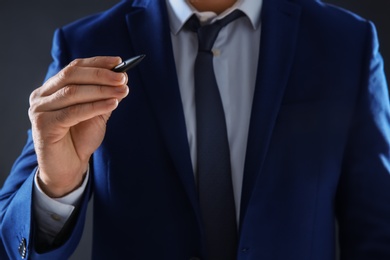 Businessman holding pen in hand on dark background