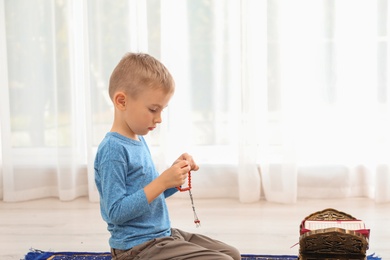 Photo of Little Muslim boy with misbaha and Koran praying on rug indoors