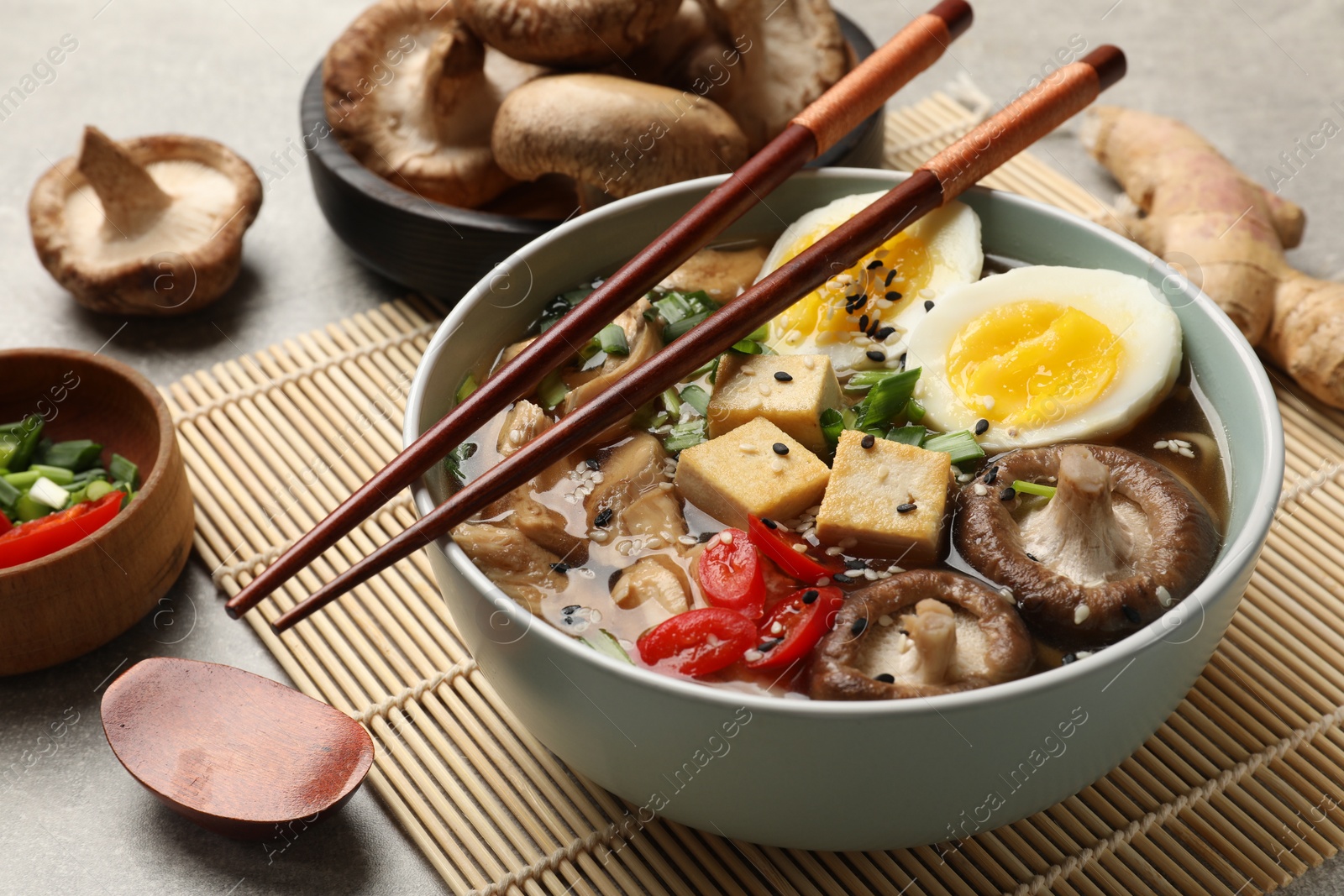 Photo of Bowl of delicious ramen and ingredients on grey table. Noodle soup