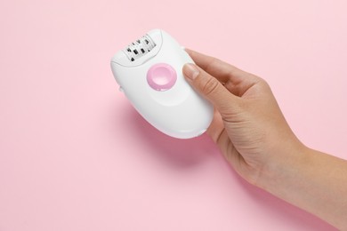 Woman holding modern epilator on pink background, top view