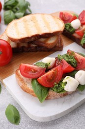 Photo of Delicious Caprese sandwiches with mozzarella, tomatoes, basil and pesto sauce on light grey table